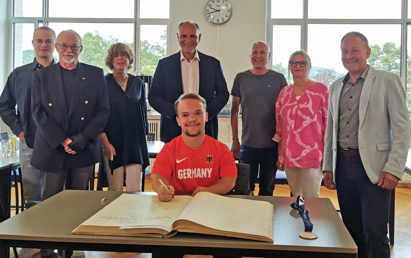 Yannis Fischer trägt sich ins Goldene Buch der Stadt Singen ein – im Beisein von (von links) seinem Bruder David, Oswald Ammon (ehemaliger Behindertenbeauftragter), Bürgermeisterin Ute Seifried, Oberbürgermeister Bernd Häusler, den Eltern Ewald und Sibylle Fischer sowie Hans-Peter Storz.