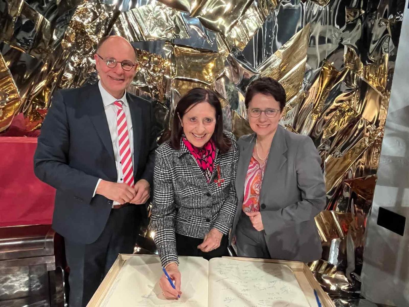 Nach der Verleihung des Bundesverdienstkreuzes trägt sich Veronika Netzhammer in das Goldene Buch der Stadt Singen ein. An ihrer Seite Justizministerin Marion Gentges und Oberbürgermeister Bernd Häusler.