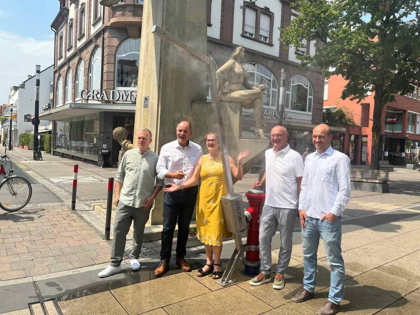 Die Nebellanzen in der Singener Innenstadt sorgen für Abkühlung. Über die Umsetzung des Projekts freuen sich (von links): Thomas Mügge (Fachbereichsleitung Bauen), Oberbürgermeister Bernd Häusler, Sandra Schupp (Stadtplanerin), Wilfried Trah (Vorsitzender von Singen Aktiv) und Tobias Herbst (Leitung Stabsstelle Klimaschutz & Klimaanpassung). Die Nebellanzen in der Singener Innenstadt sorgen für Abkühlung. Über die Umsetzung des Projekts freuen sich (von links): Thomas Mügge (Fachbereichsleitung Bauen), Oberbürgermeister Bernd Häusler, Sandra Schupp (Stadtplanerin), Wilfried Trah (Vorsitzender von Singen Aktiv) und Tobias Herbst (Leitung Stabsstelle Klimaschutz & Klimaanpassung).